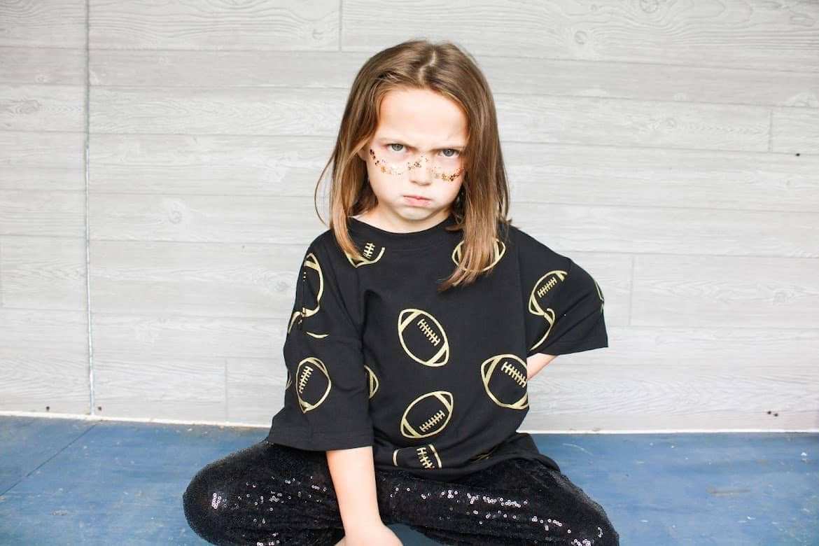 Girls wearing oversized black and gold game day tee with football design.