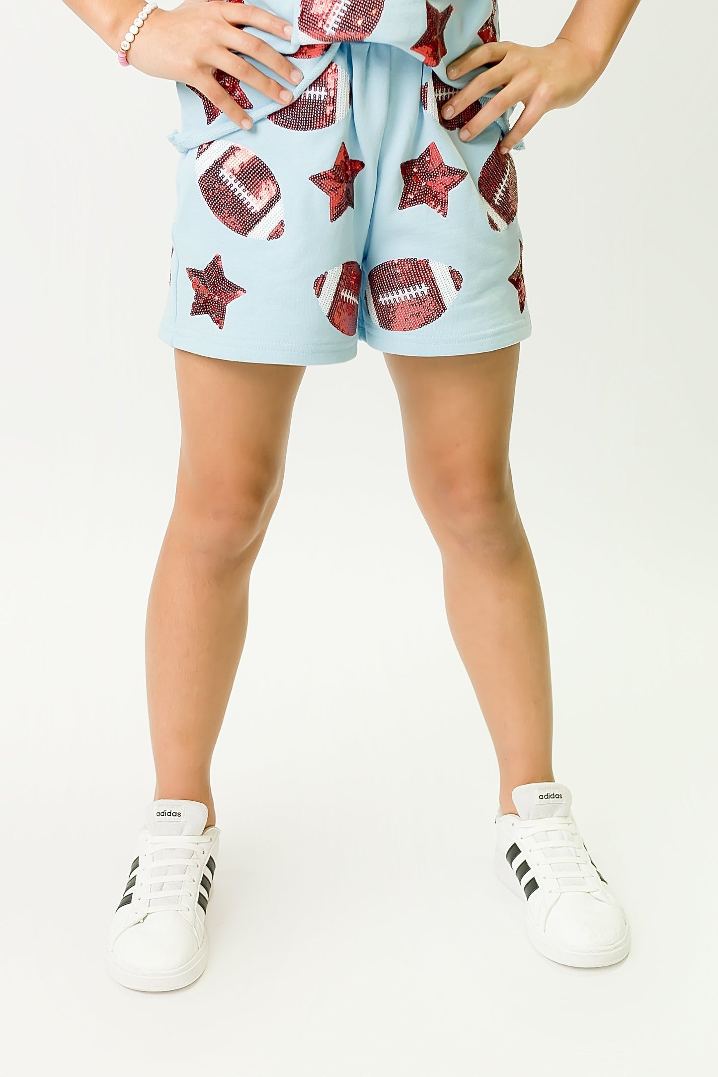 Light blue football shorts with football and star patterns worn by a child with white sneakers
