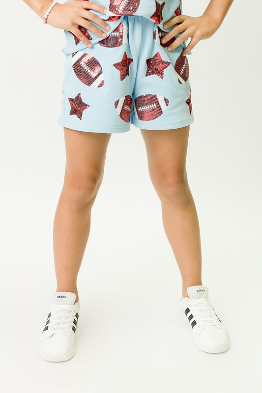 Light blue football shorts with football and star patterns worn by a child with white sneakers