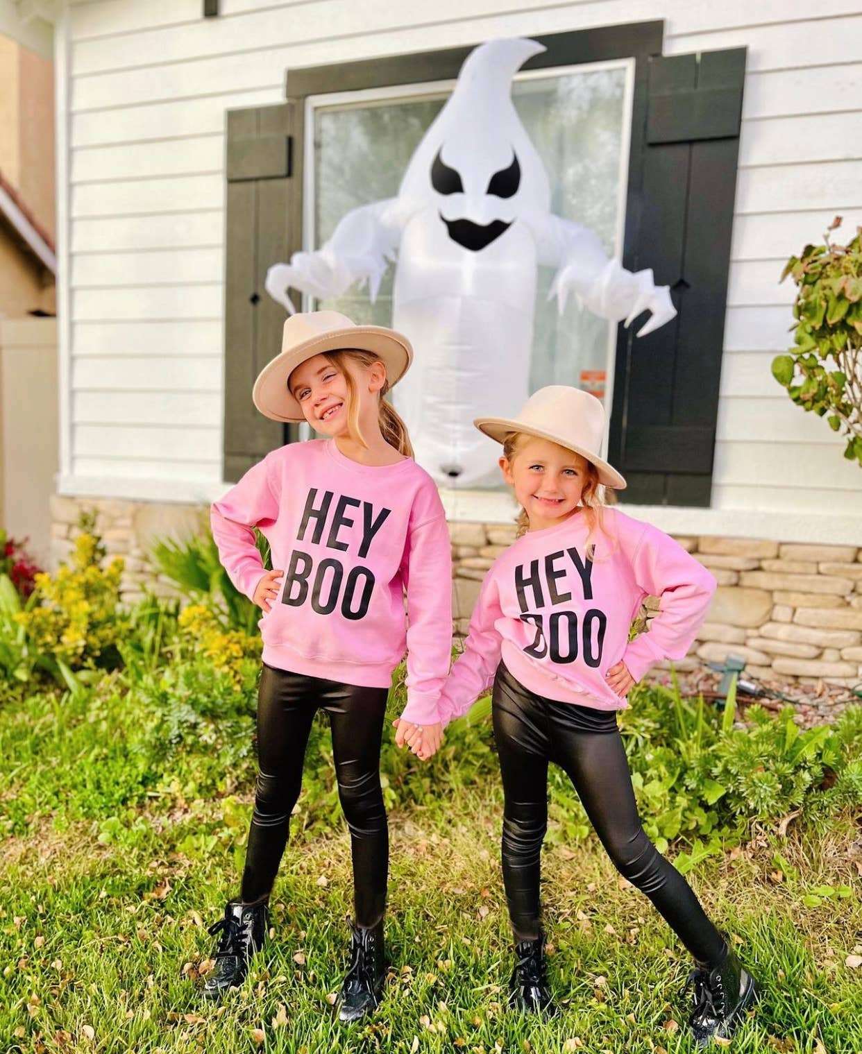 Kids wearing pink "Hey Boo" Halloween sweatshirts from Holland Ave Clothing standing in front of Halloween decor.