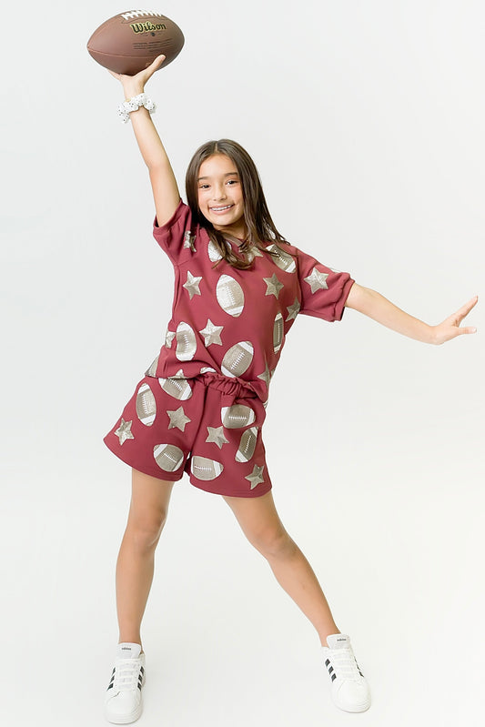 Young girl in maroon football top with star and ball prints holding a football and smiling