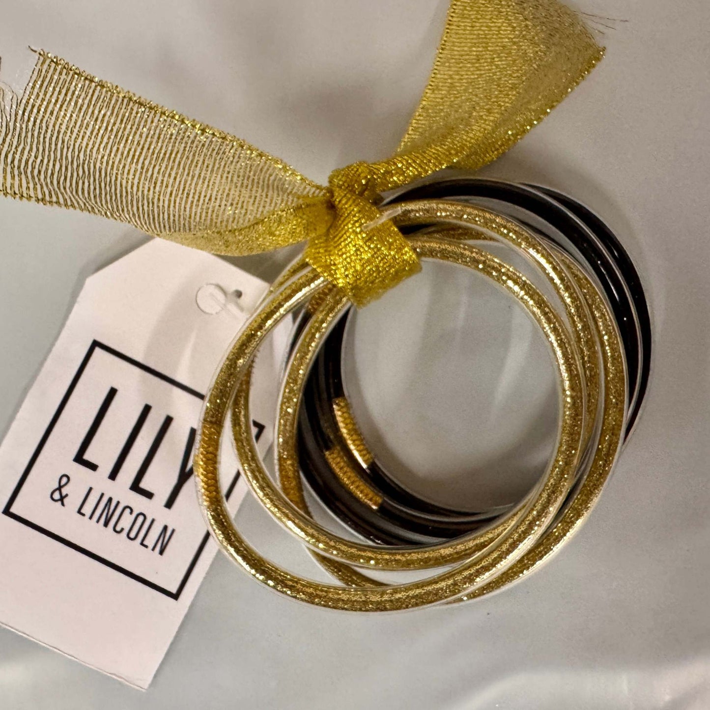 Gold bangles with a gold ribbon and 'LILY & LINCOLN' tag on a white background