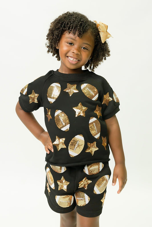 Child wearing black football top with gold sequin football and star designs paired with matching shorts