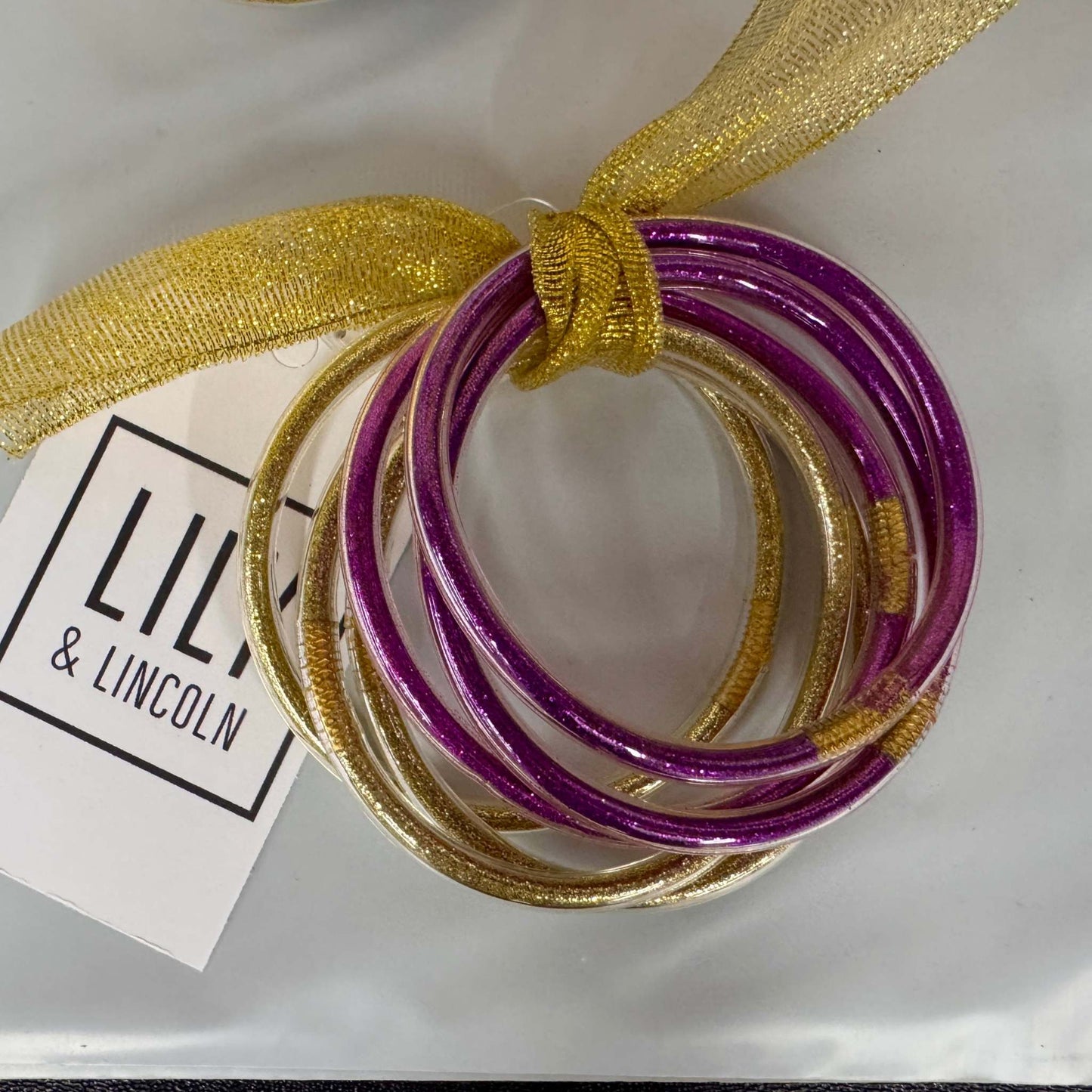 Set of purple and gold bangles with a gold ribbon on a white background, featuring a 'LILY & LINCOLN' tag.