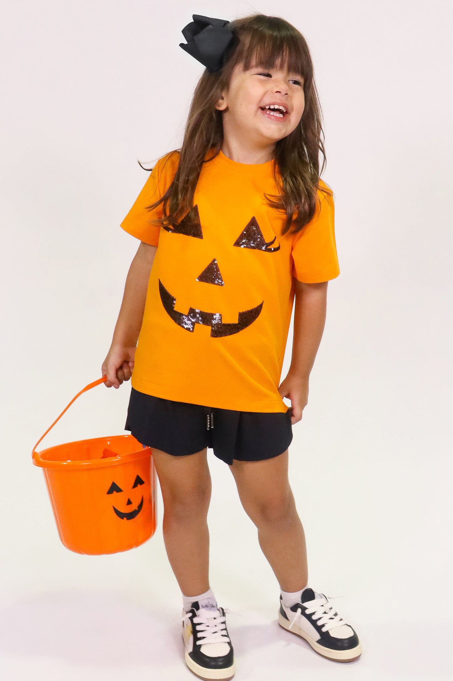 Toddler wearing orange Jack O Lantern Shirt with sequin face design holding Halloween bucket
