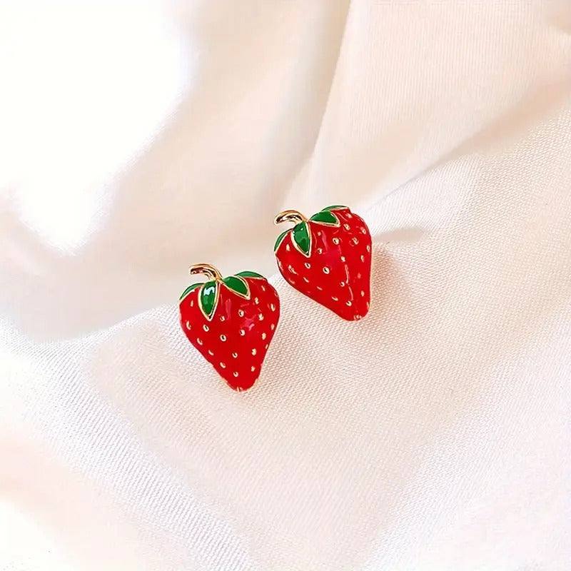 Beautiful strawberry stud earrings on white fabric background.
