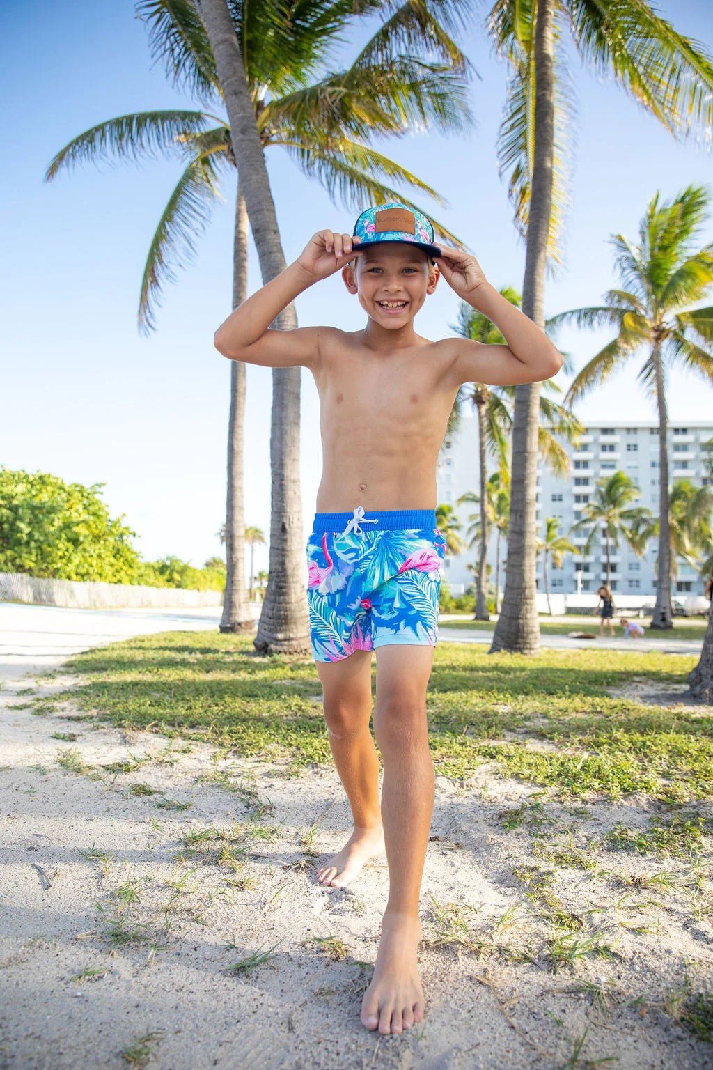 Boy wearing Blueberry Bay Indigo Flamingo Swim Trunks, beach setting.