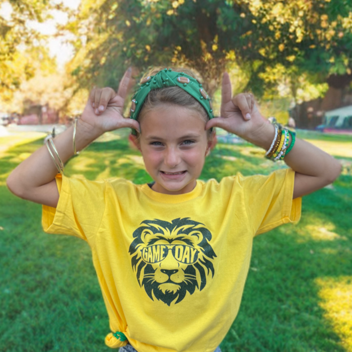 Child wearing a yellow t-shirt with a lion graphic in a park