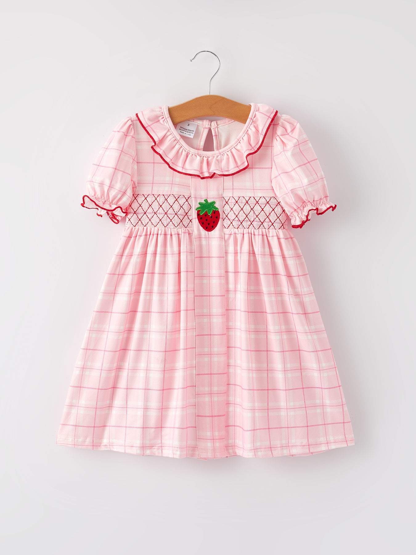 Pink checkered dress with strawberry design on a hanger against a white background