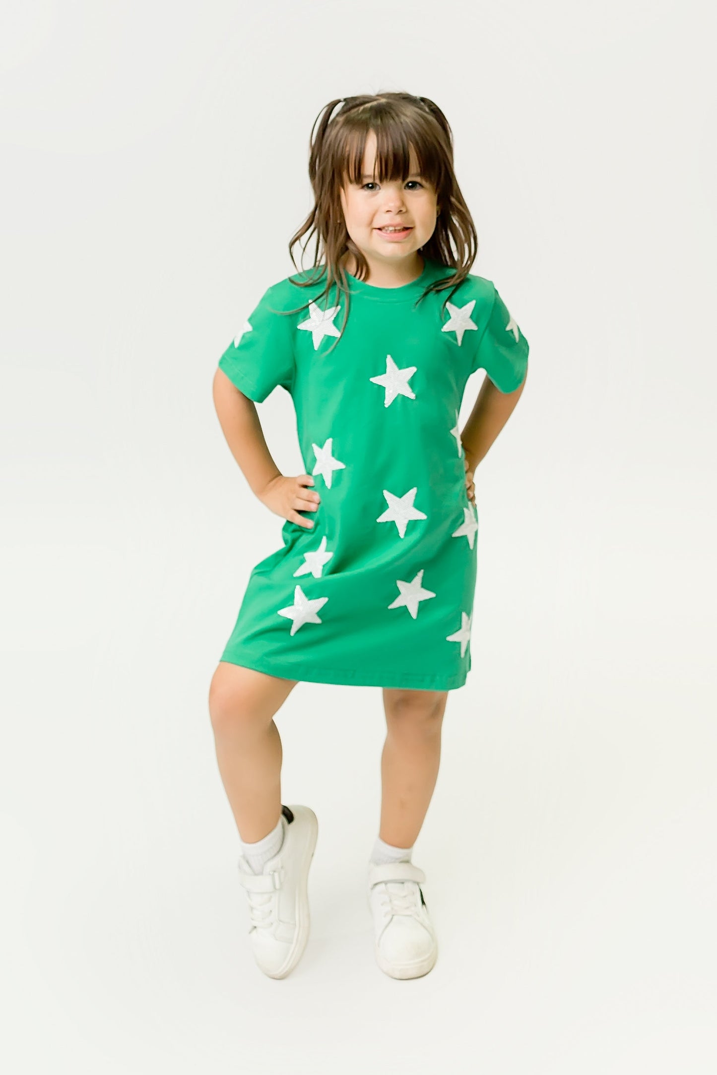 Little girl wearing vibrant Green Star Dress with white stars and white sneakers standing confidently
