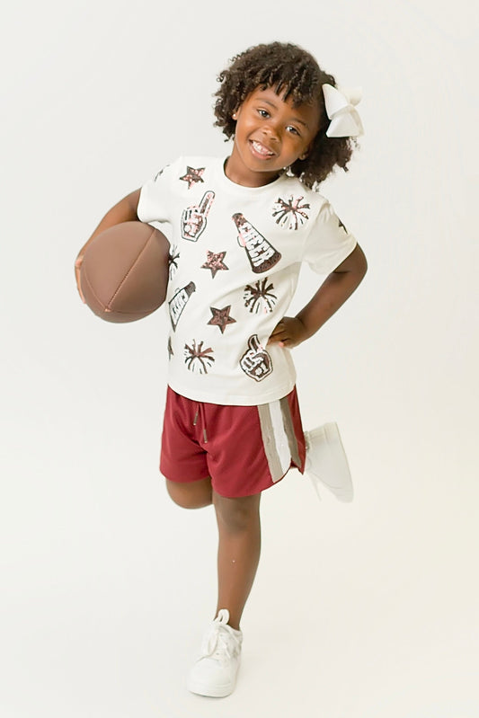 Child wearing maroon and white cheer shirt holding football and smiling