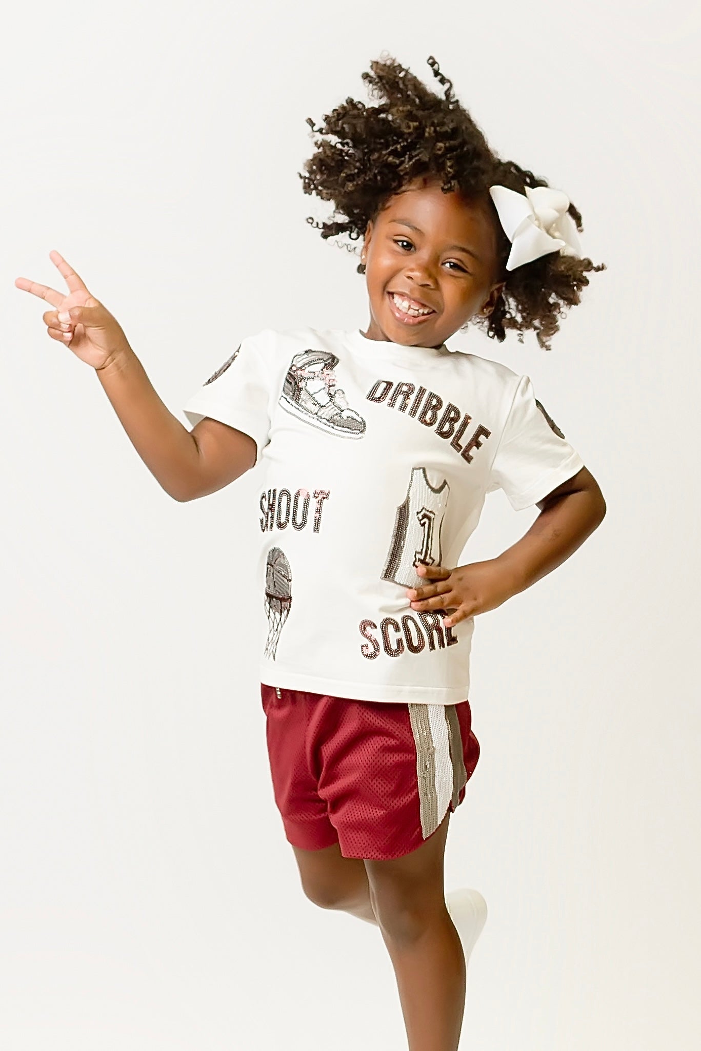 Child wearing maroon basketball shorts and white sports shirt playing basketball