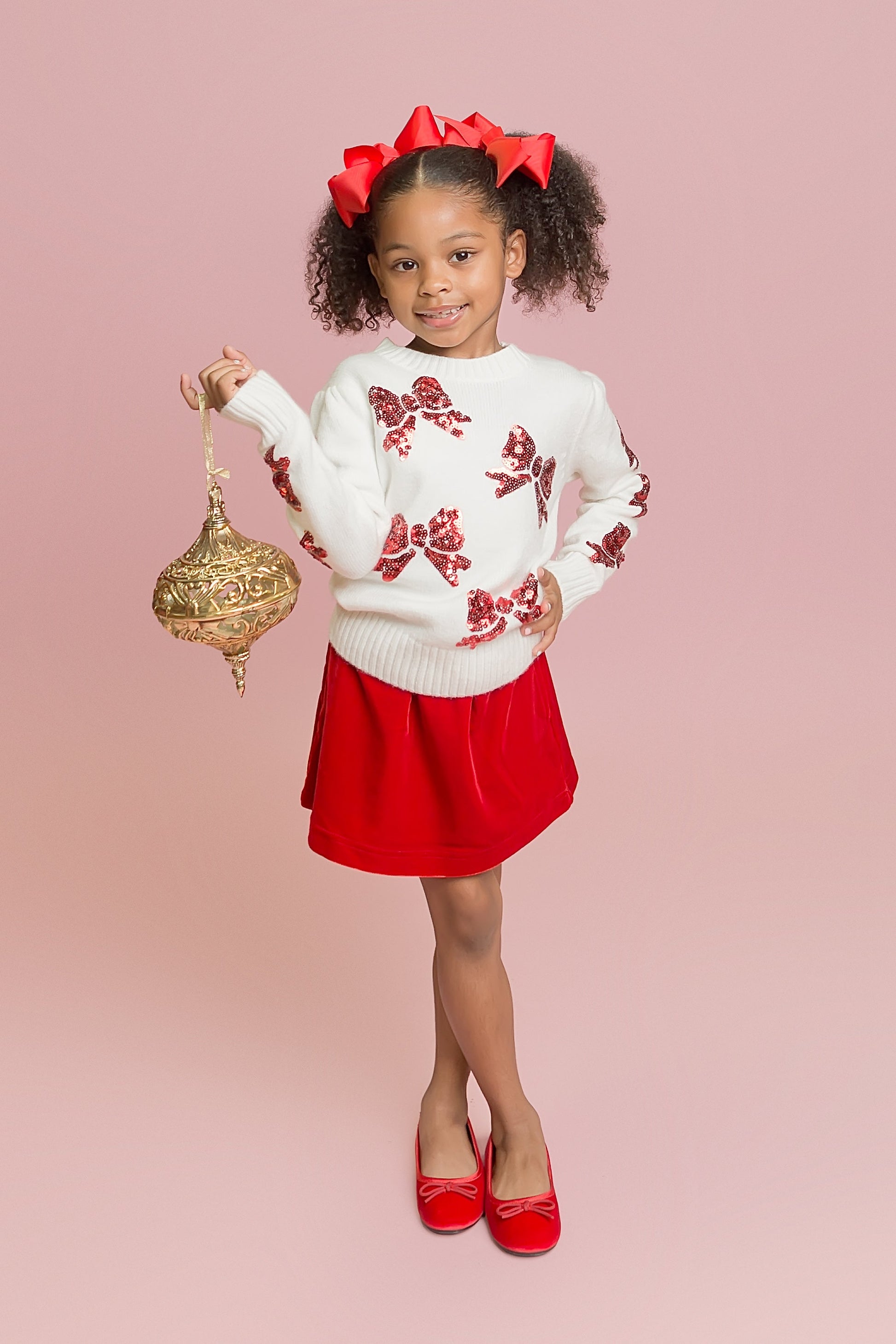 Young girl in a white sweater with red floral patterns and a red skirt holding a gold lantern on a pink background