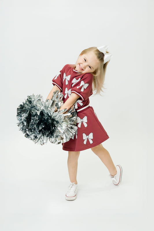 Girl wearing maroon and white bows top and skirt with pom-poms cheering