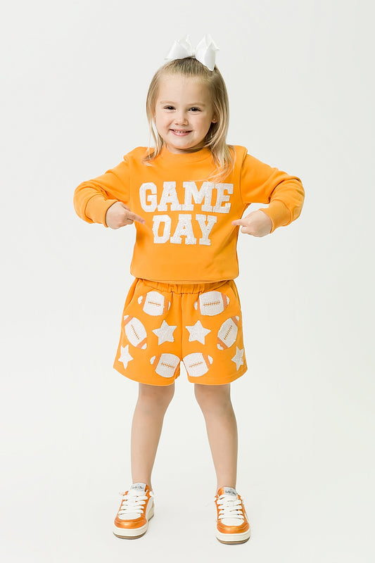 Little girl wearing vibrant orange gameday sweatshirt and matching skirt with football and star prints.