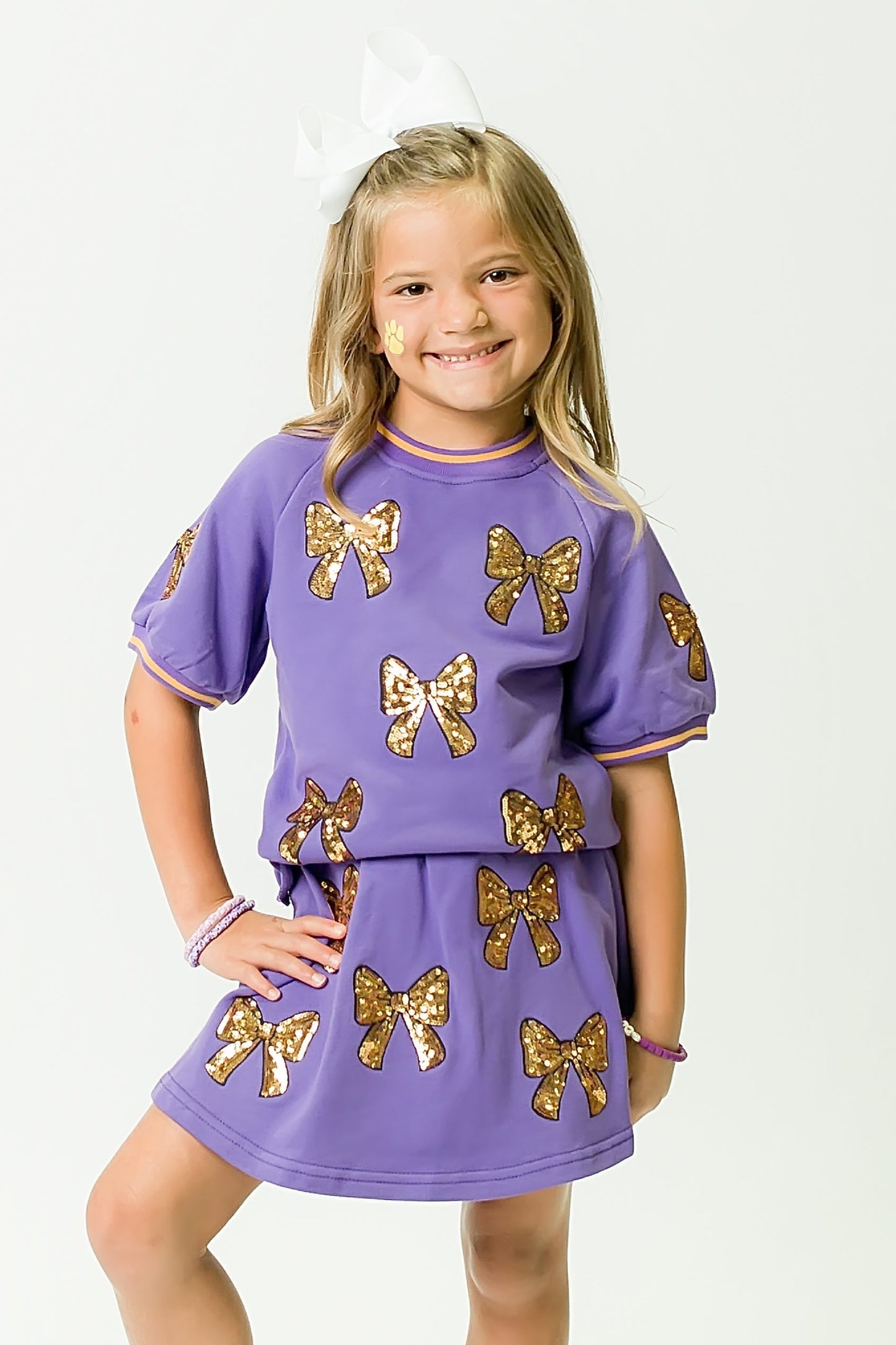 Girl wearing purple and gold bows top and matching skirt with sequin bow designs