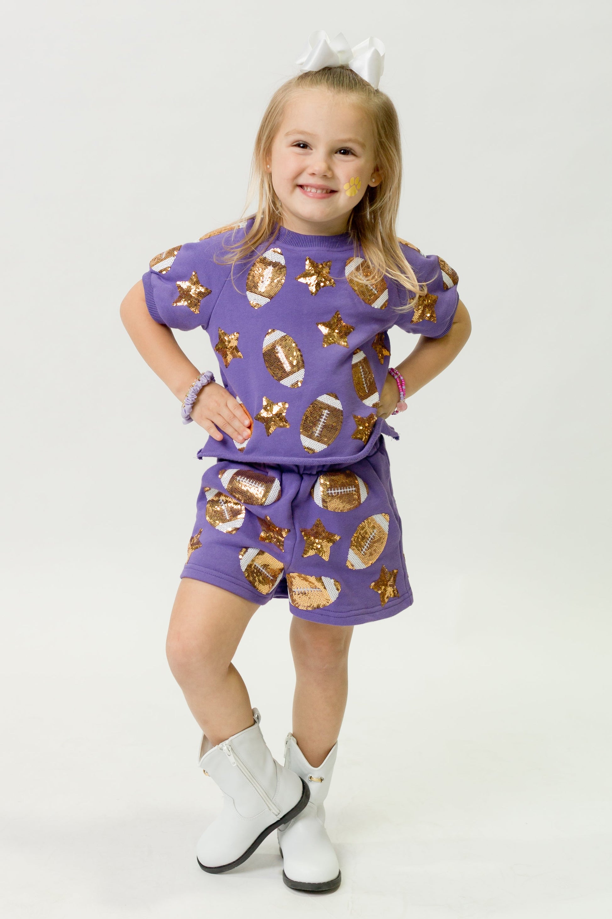 Young girl wearing a vibrant purple football top and matching shorts with gold stars and football patterns.