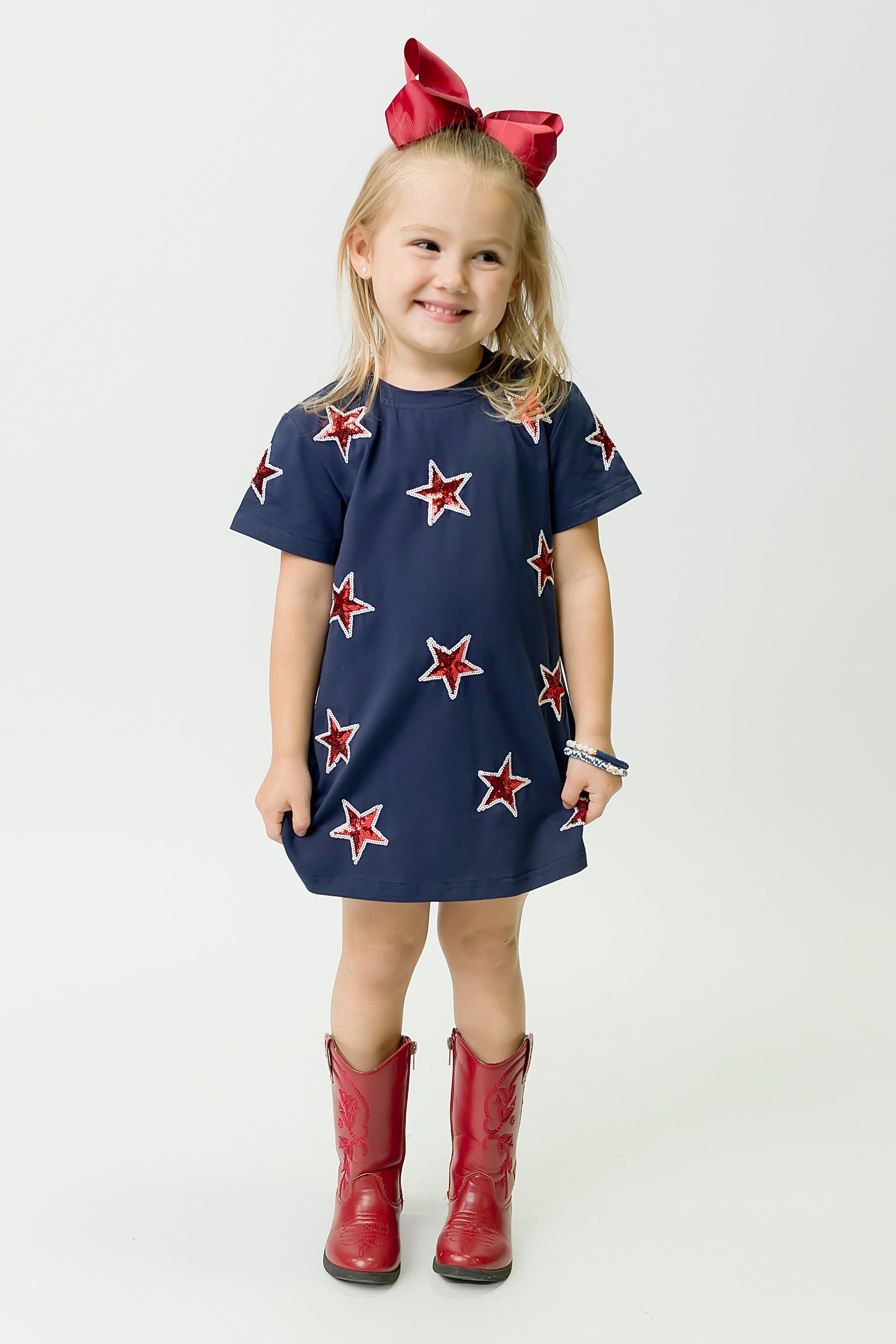 Young girl wearing navy and red star dress with red boots and bow