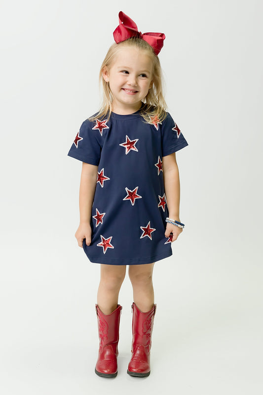 Young girl wearing navy and red star dress with red boots and bow