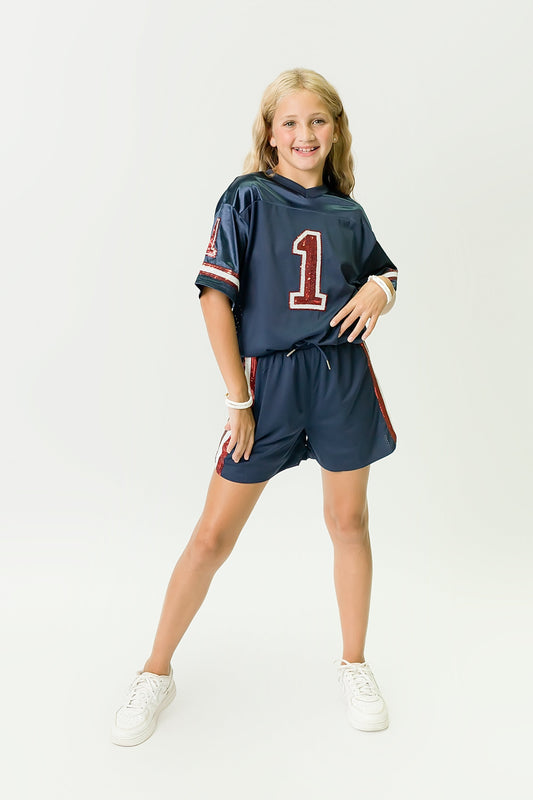 Girl wearing navy blue and red sequin jersey with number 1 and matching shorts standing confidently
