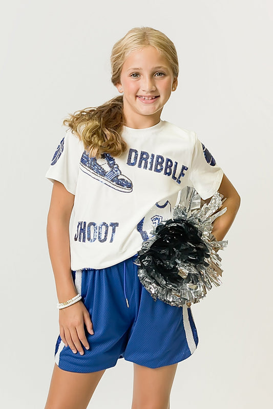 young girl wearing royal blue basketball shorts and white graphic shirt holding black and silver pom pom
