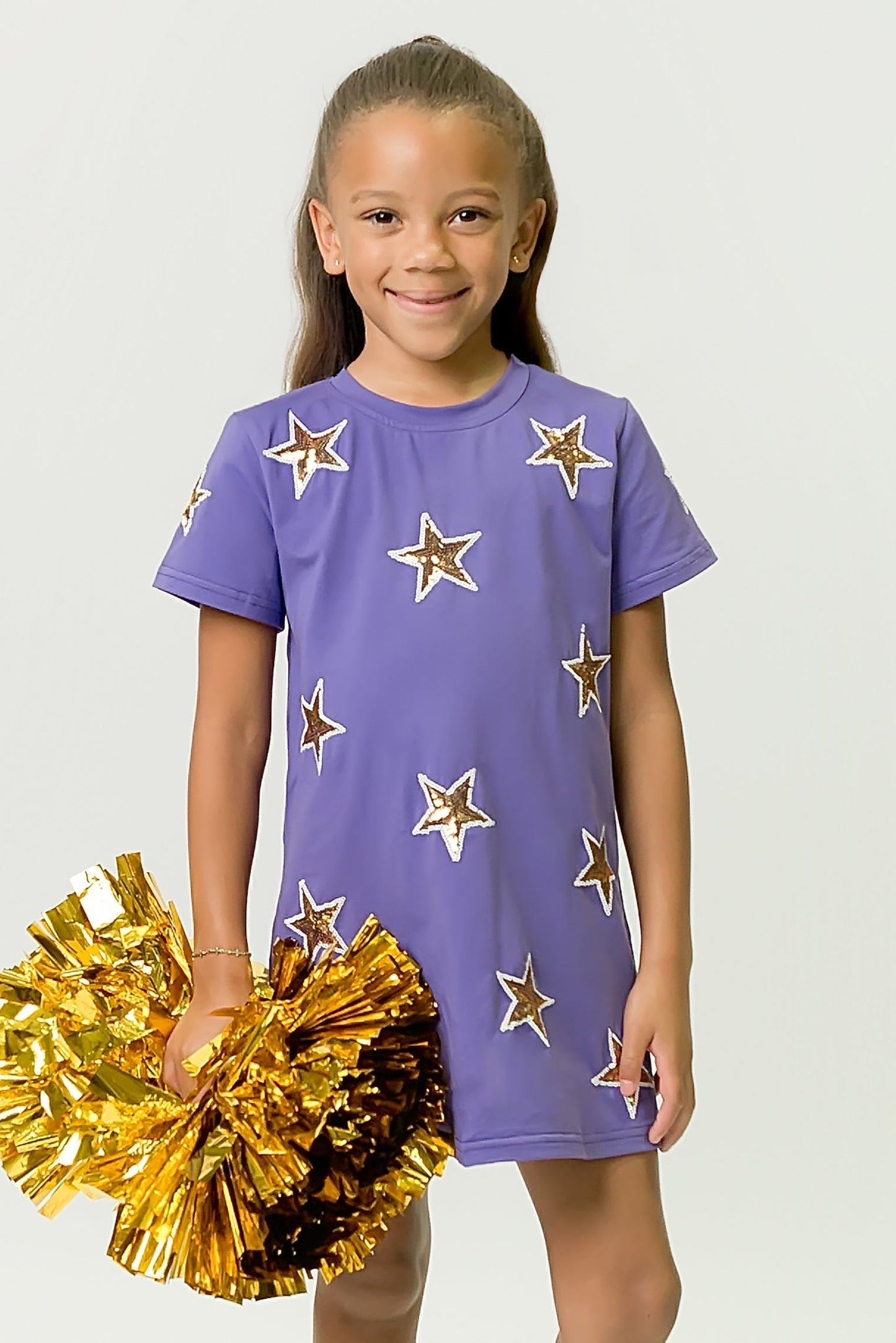 Girl wearing purple and gold star dress holding gold pom-poms