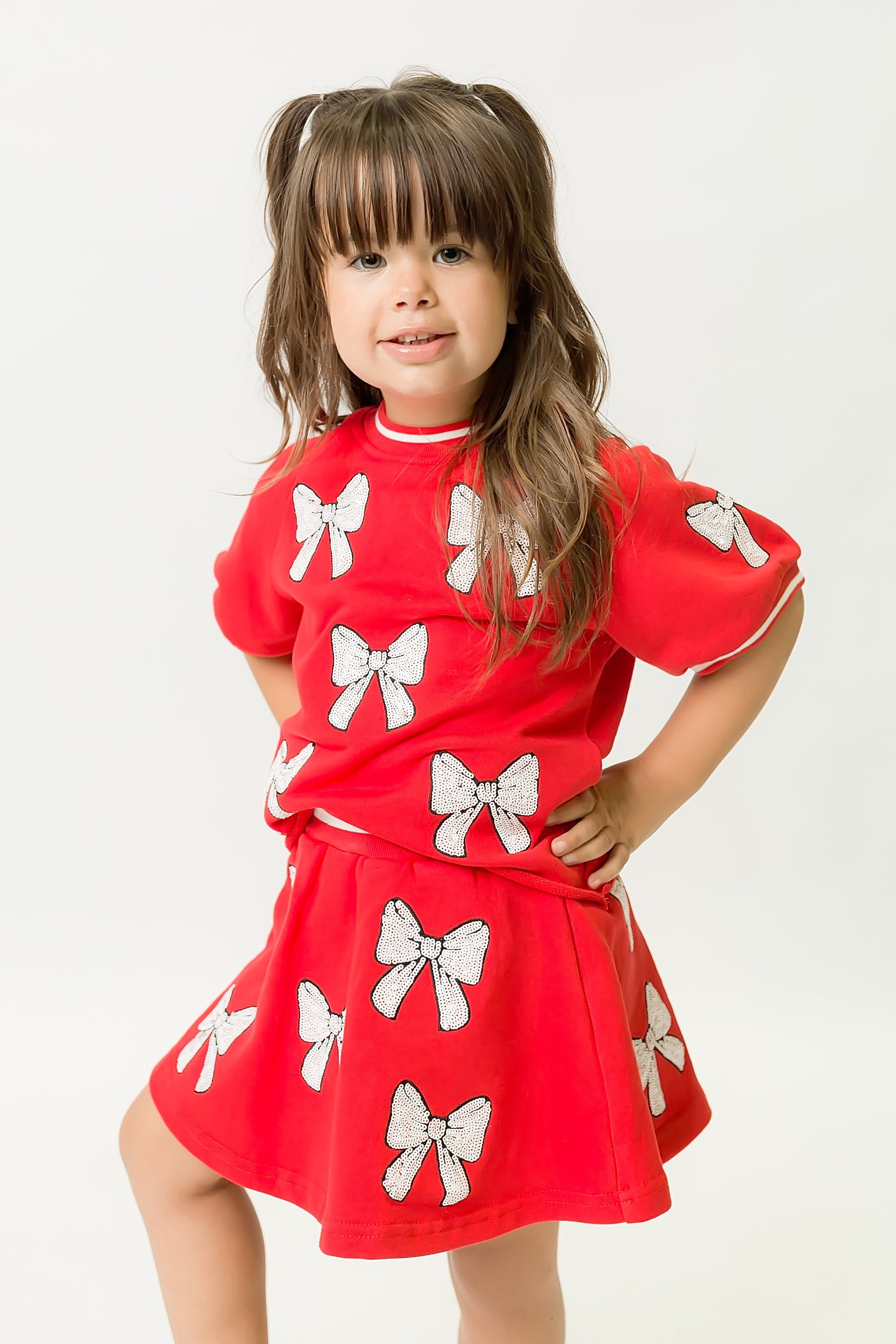 Toddler wearing red and white bows top with sequin bow details and matching skirt against a white background