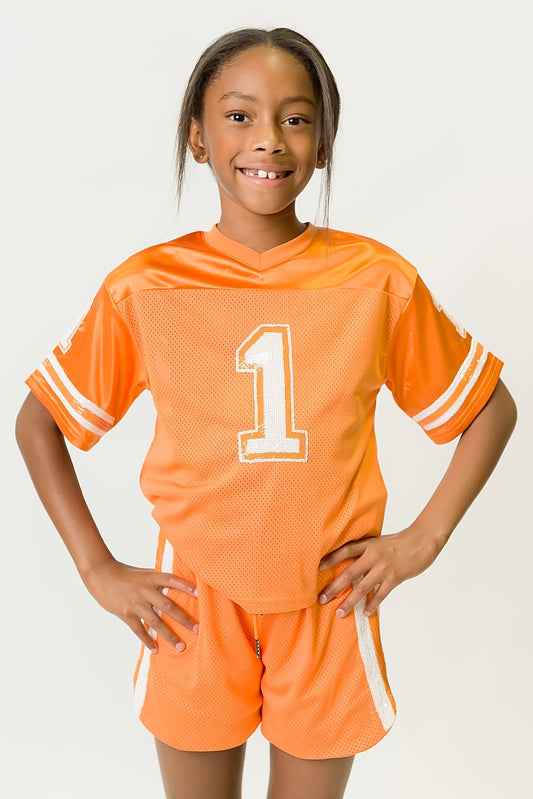 girl wearing orange and white sequin jersey with number one and matching shorts smiling