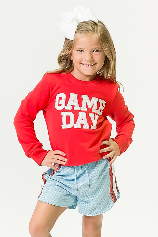 Girl wearing red gameday sweatshirt with white lettering and light blue shorts