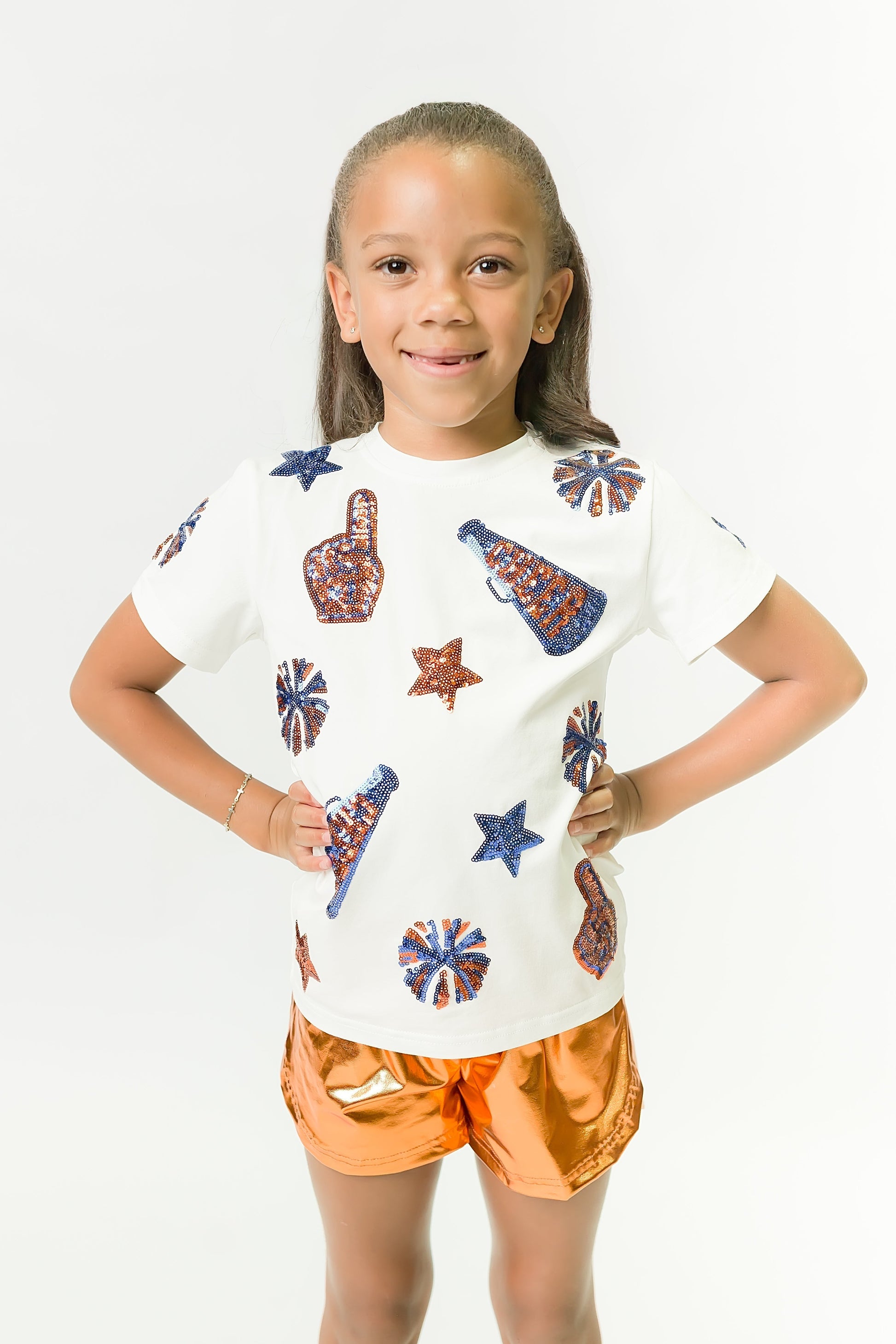 Child wearing royal and orange cheer shirt with foam finger and pom-pom designs