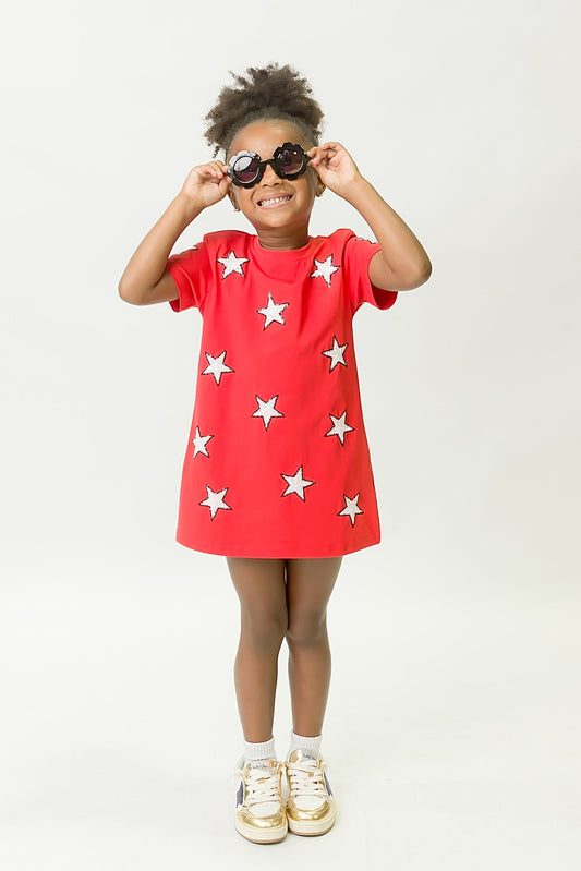 Child wearing playful red and black star dress with white star patterns and gold shoes