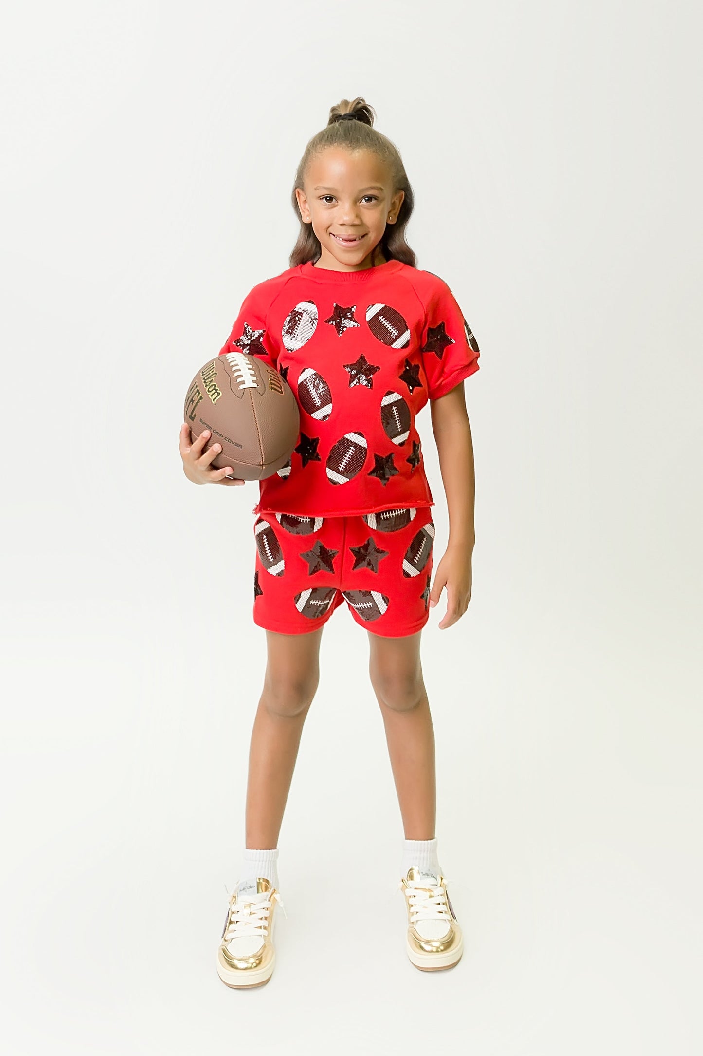Child wearing red and black football top and matching shorts holding a football