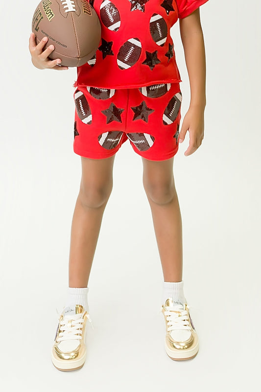 Child wearing red and black football shorts with football and star patterns holding a football