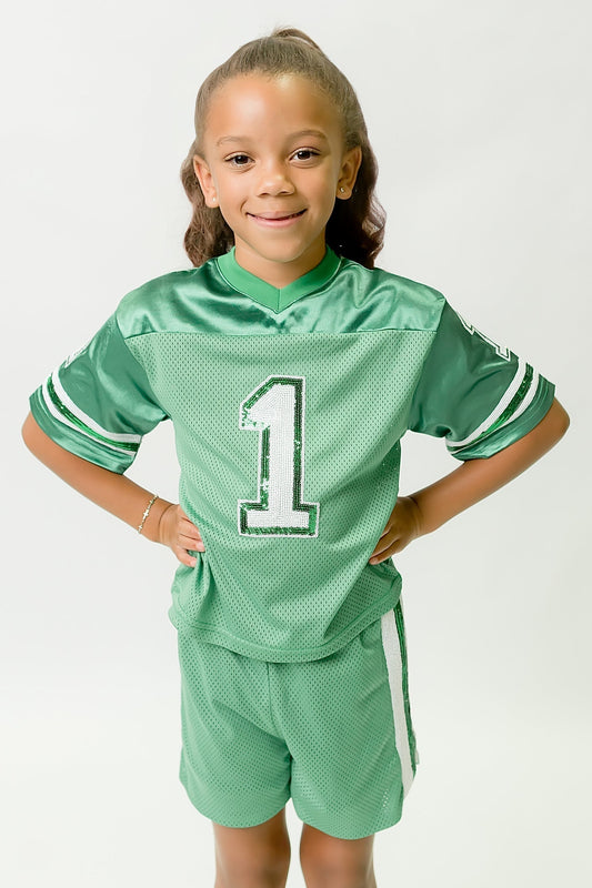 Young girl wearing green and white sequin jersey with number 1 standing with hands on hips