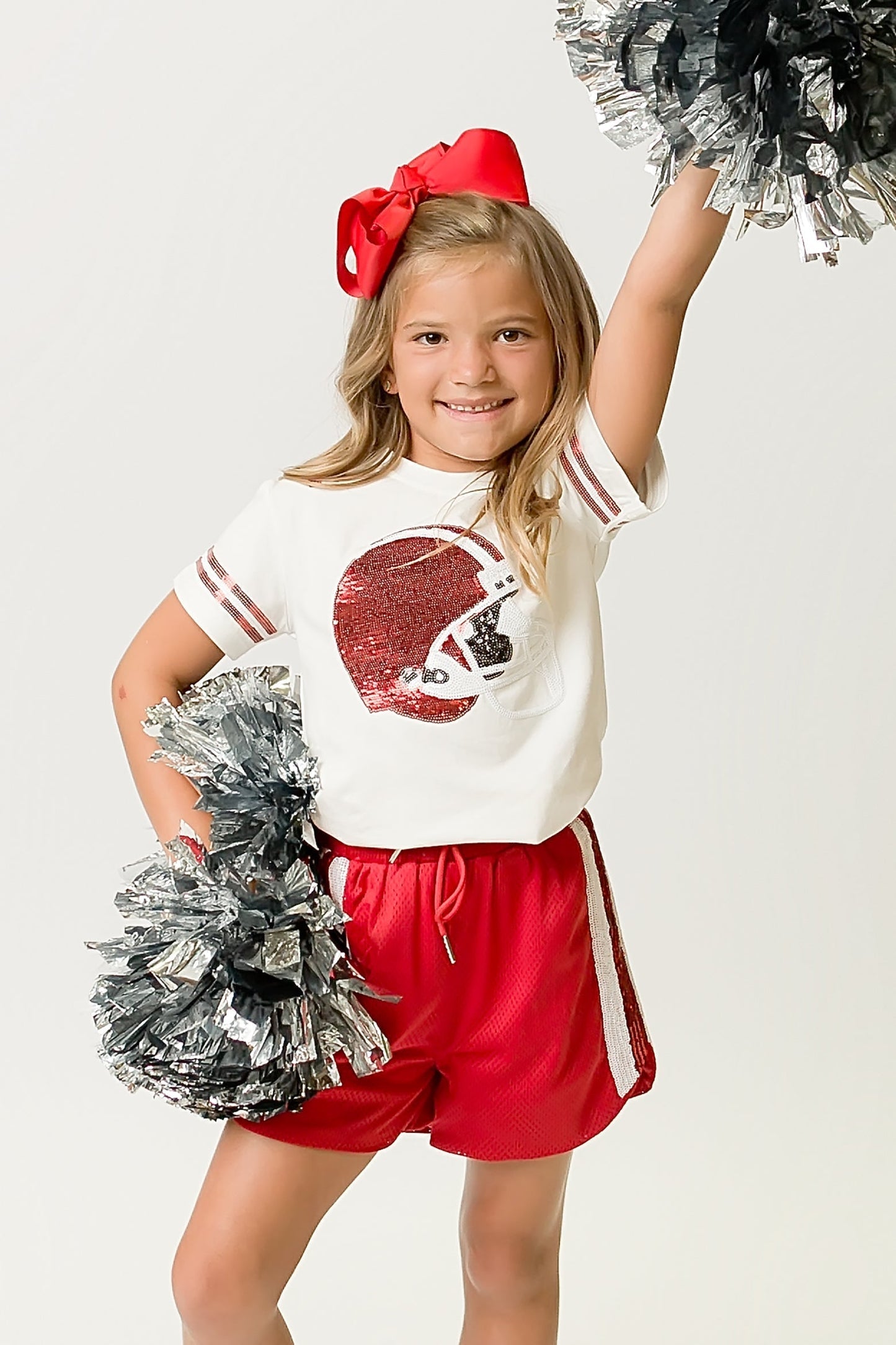 Young girl wearing a Red Helmet Shirt with red sequin football helmet design and matching red shorts cheering with pom-poms