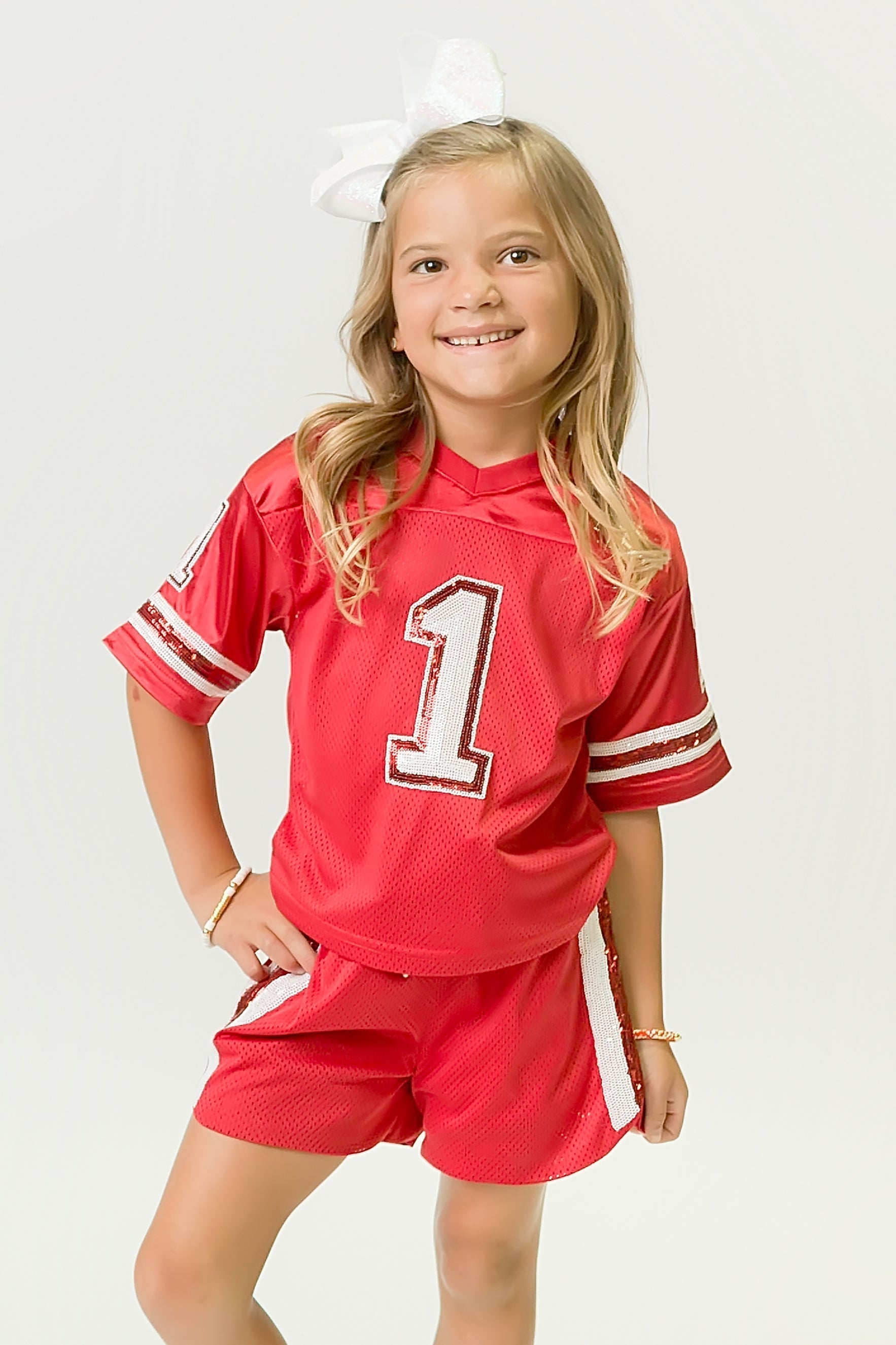 Girl wearing a red and white sequin jersey with matching shorts and white bow in hair
