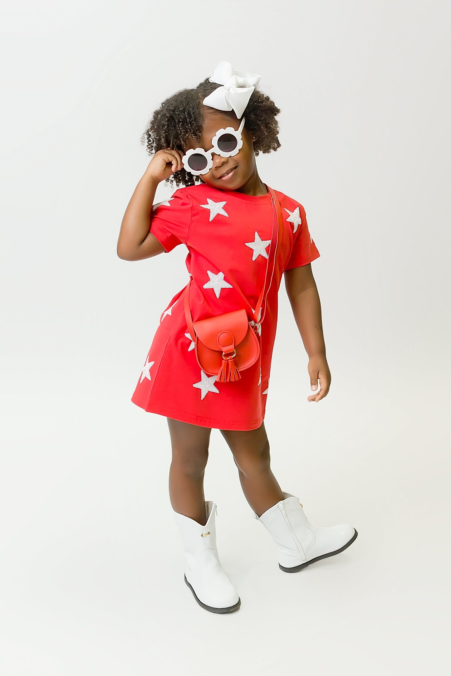 Girl wearing a vibrant red star dress with white stars, white boots, and sunglasses
