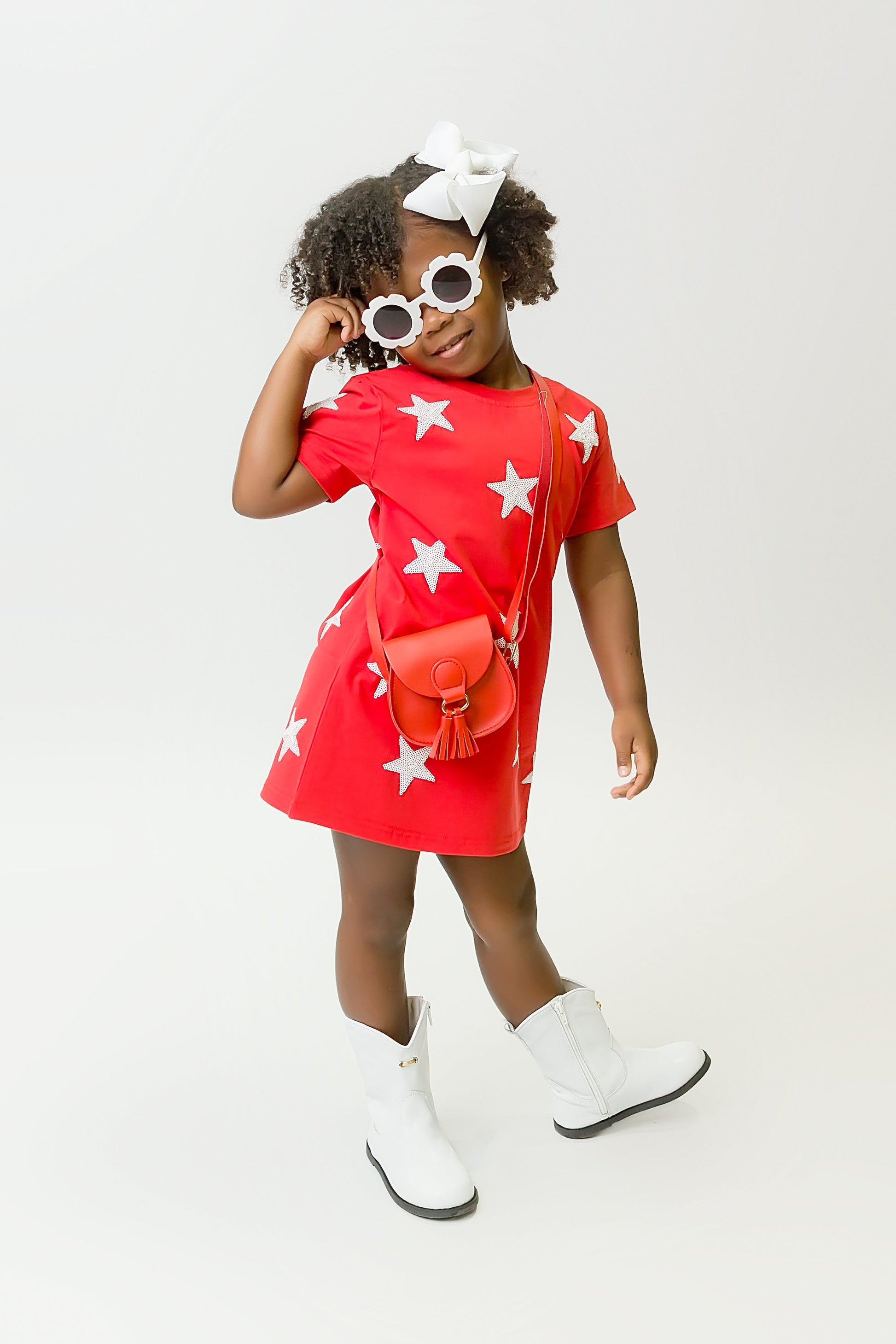Girl wearing a vibrant red star dress with white stars, white boots, and sunglasses
