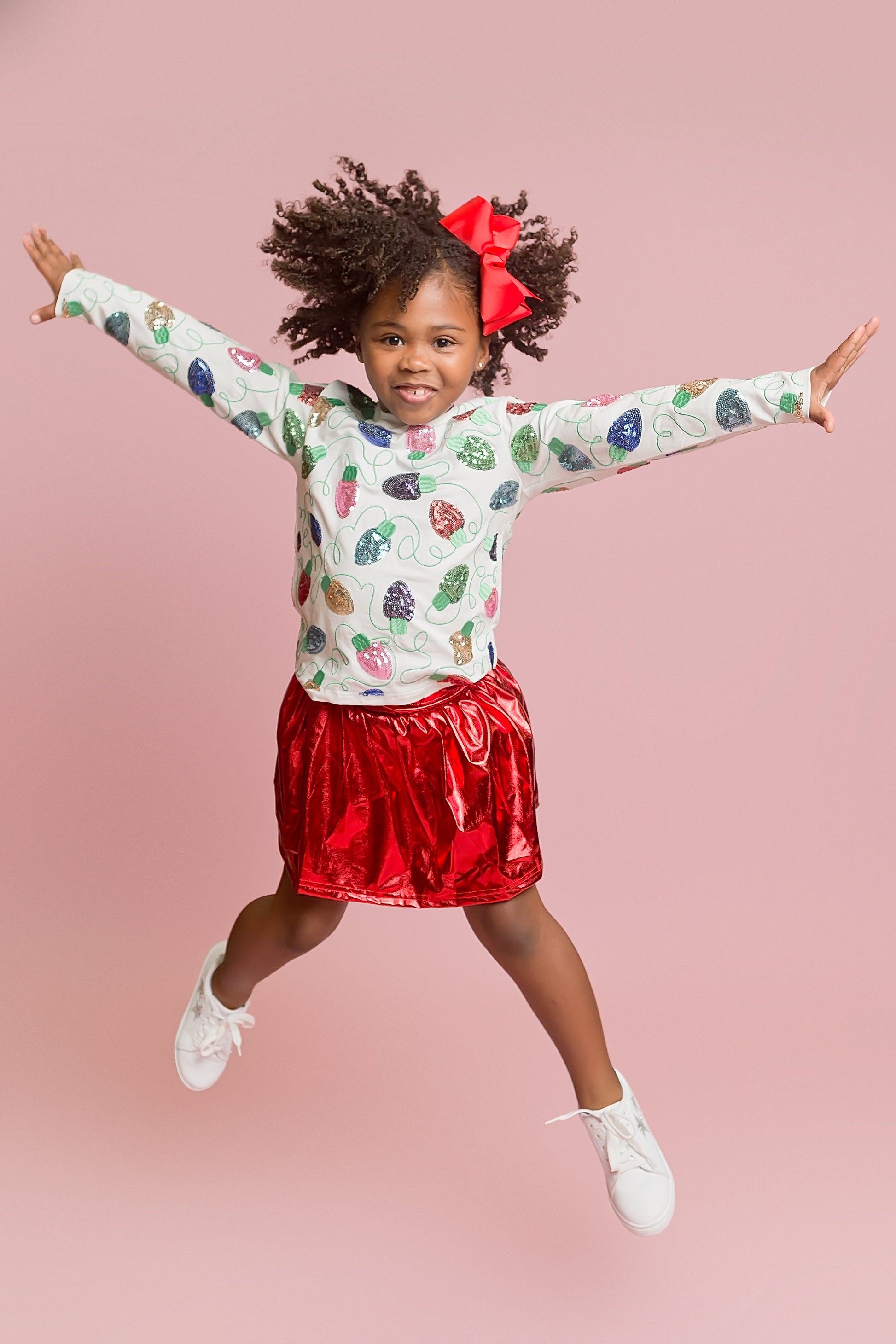 Child wearing a colorful long-sleeve shirt and red skirt on a pink background