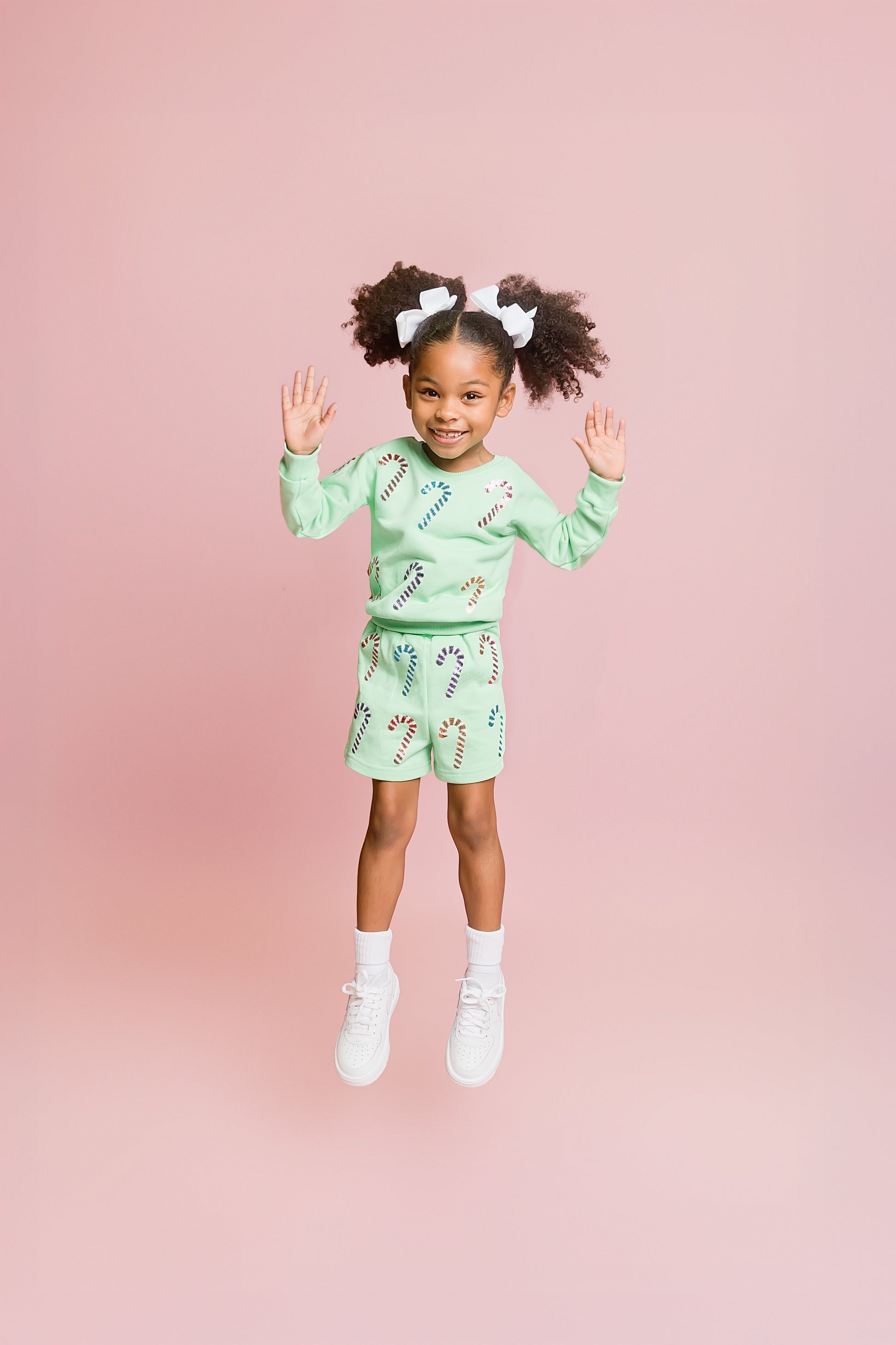 Child wearing a green outfit with candy cane patterns on a pink background