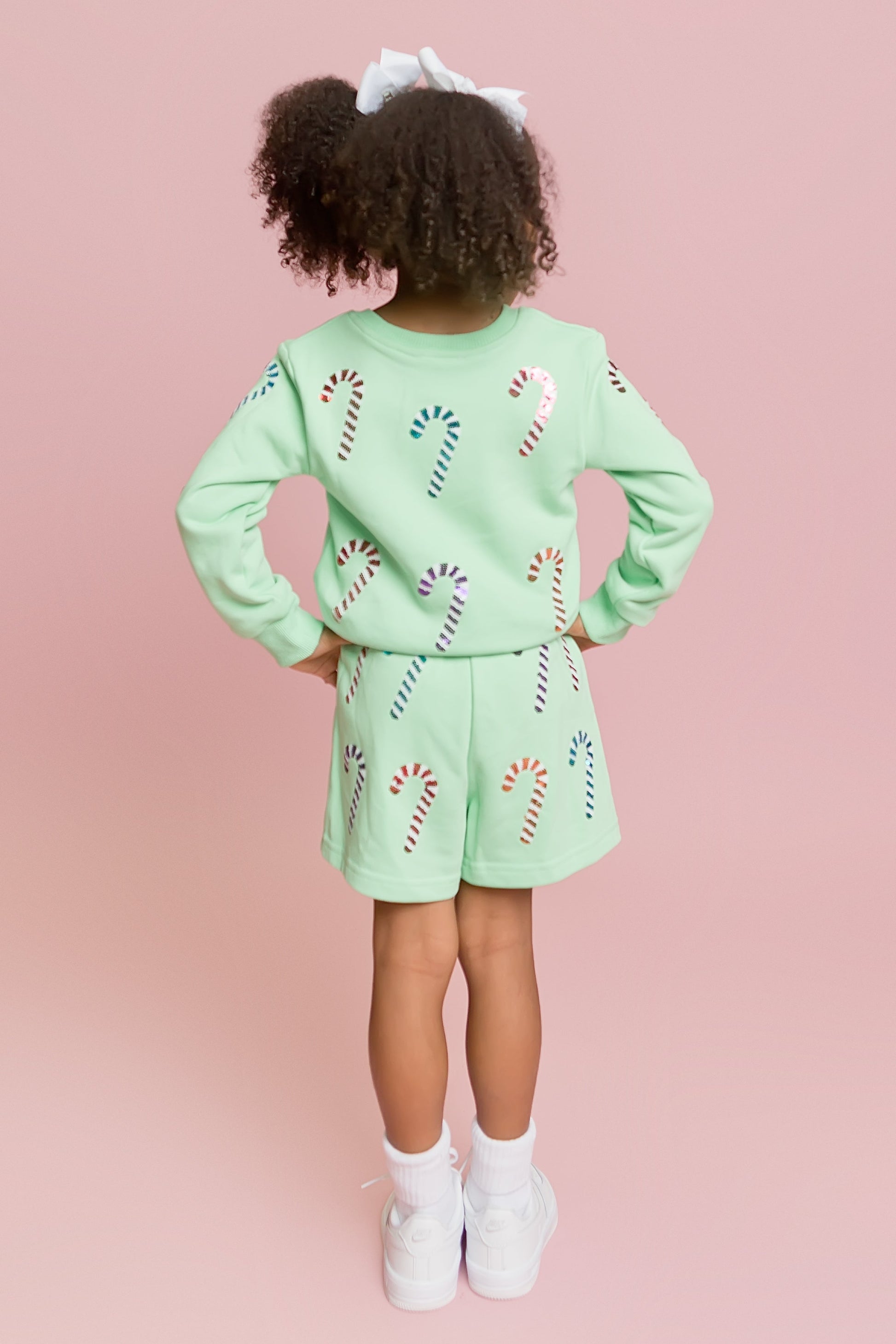 Child wearing a light green outfit with candy cane patterns on a pink background