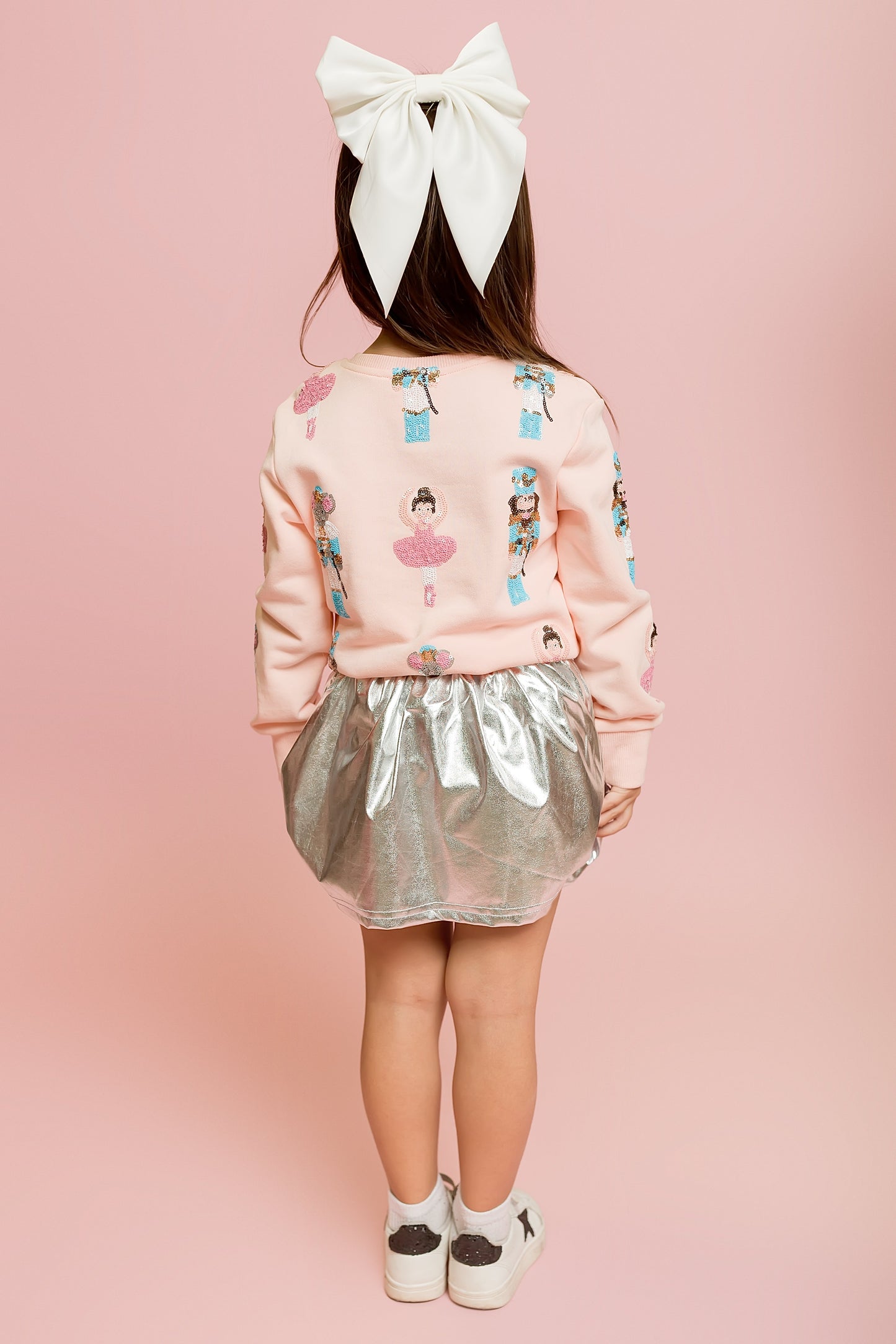 Child wearing a pink jacket with character designs and a silver skirt on a pink background