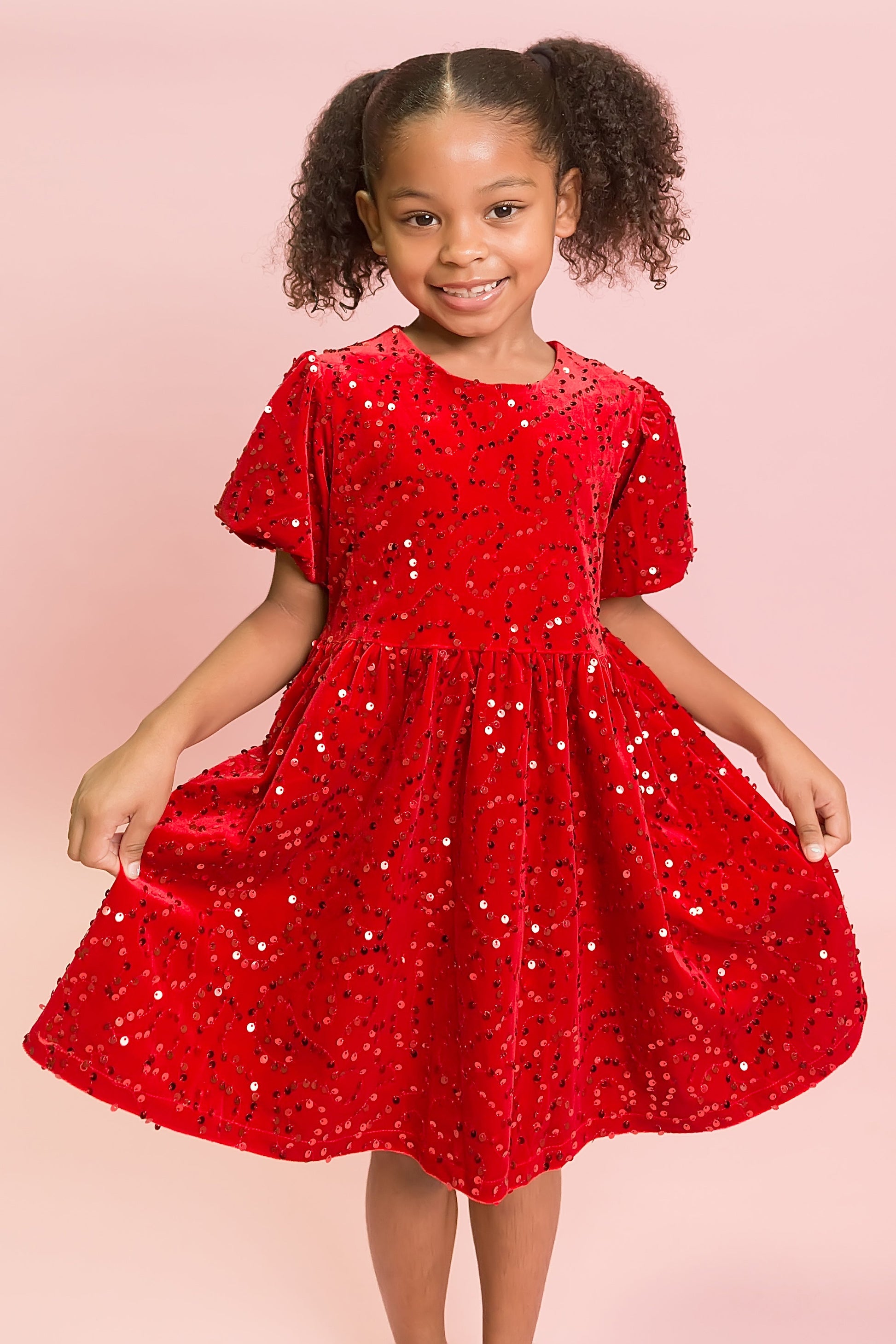 Young girl wearing a red sequin dress on a pink background