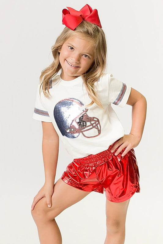 Young girl wearing light blue and red helmet shirt with red shorts and bow