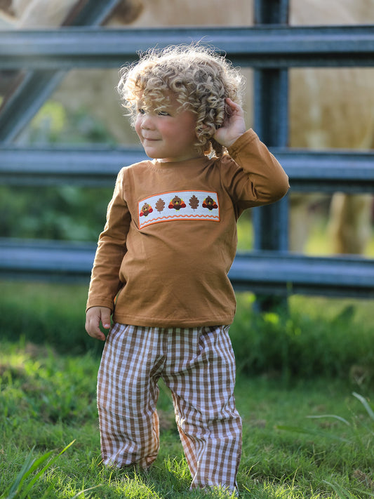 Child wearing a brown shirt with a pattern and checkered pants standing outdoors.