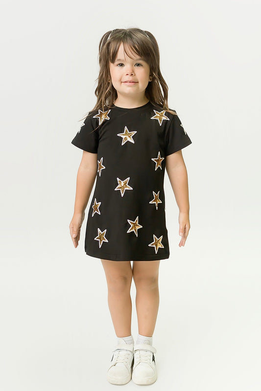 Little girl wearing black and gold star dress with white sneakers against white background