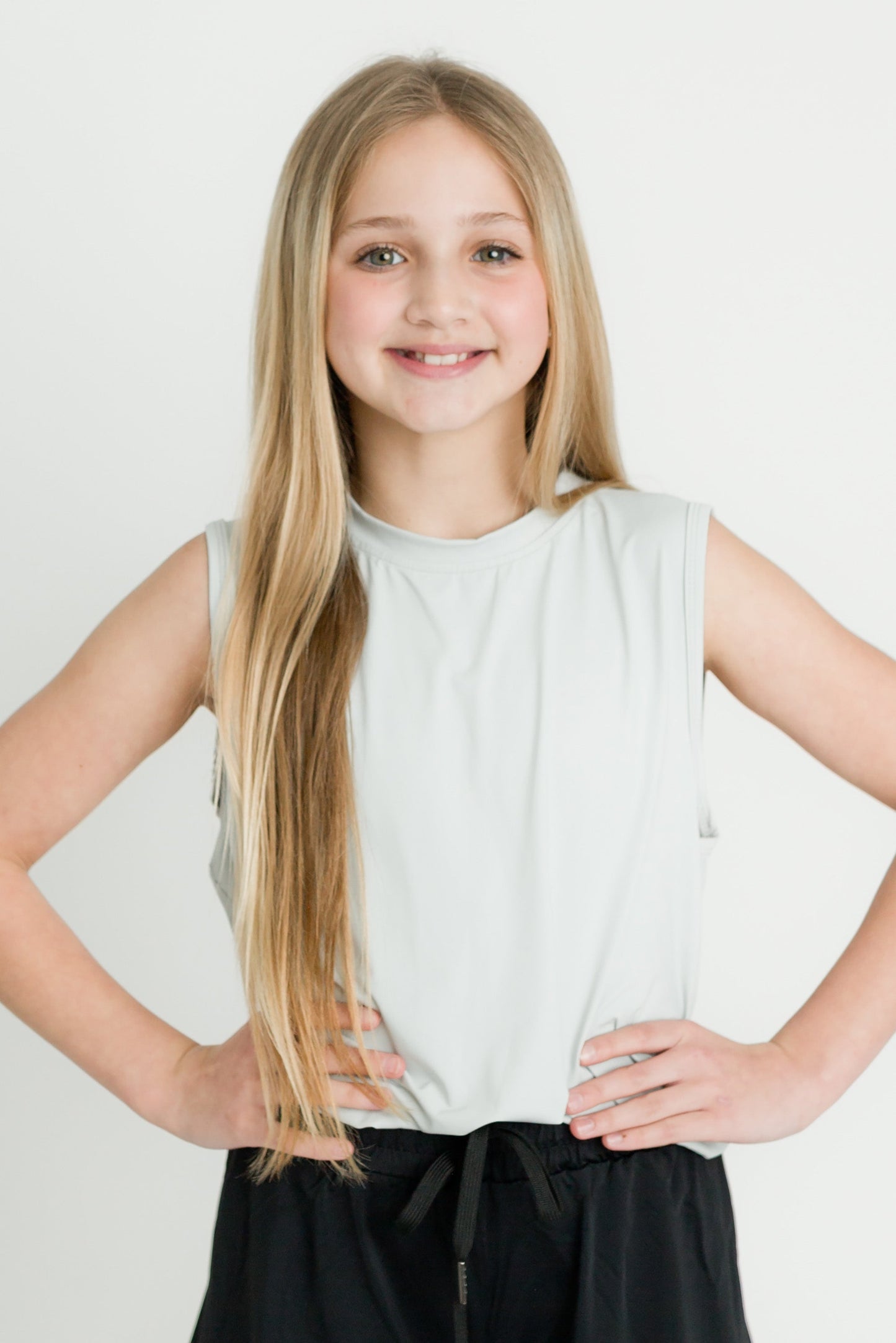 Girl wearing gray high low kid tank with black pants smiling with hands on hips