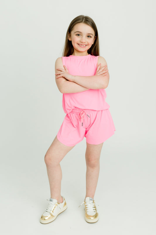 Young girl wearing hot pink kid butterfly shorts with a matching top and white sneakers