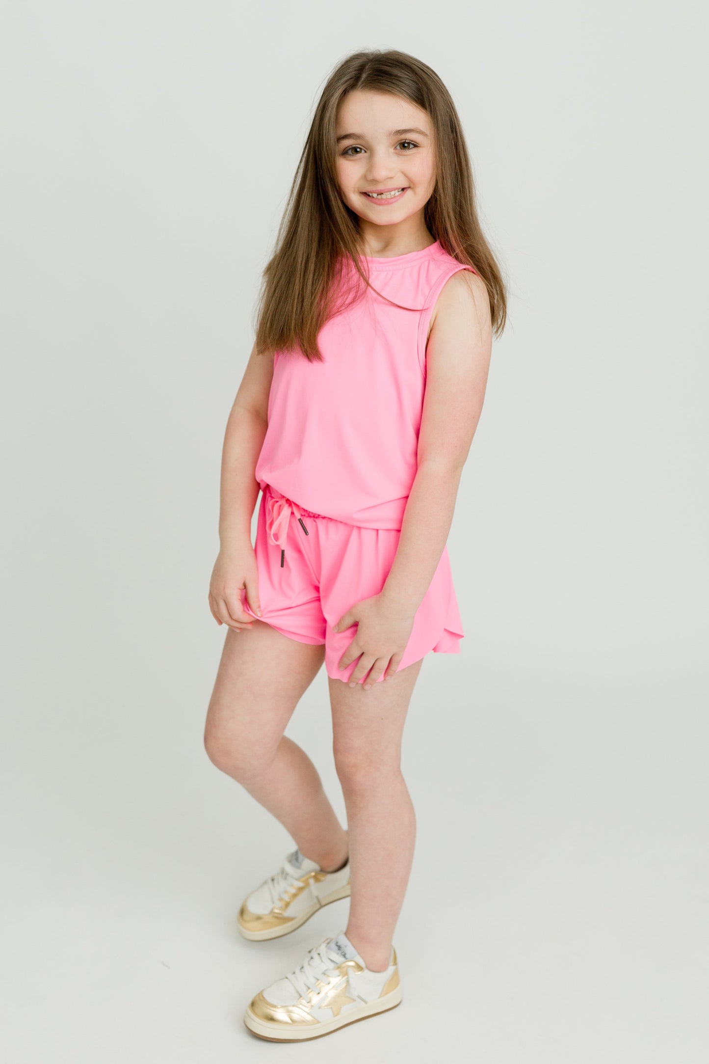 Girl wearing hot pink high low kid tank with matching shorts and sneakers