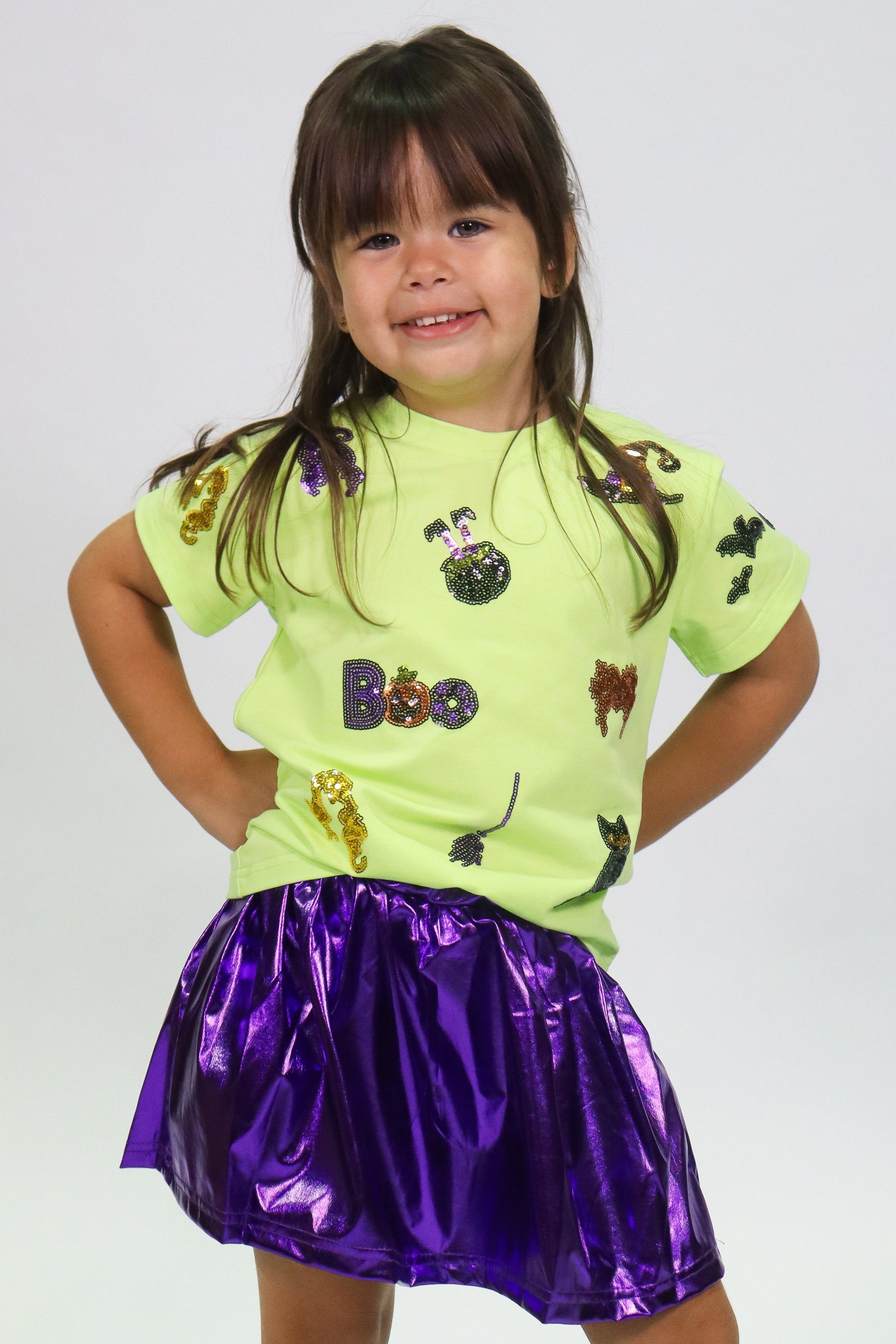 Smiling child wearing a Halloween Icon Shirt with sequins and a shiny purple skirt.